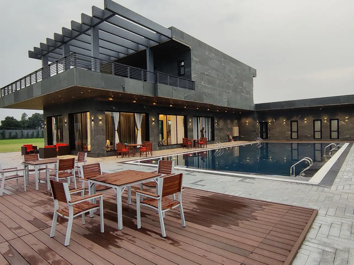 Timber deck and dining tables beside the pool, with the house lit behind
