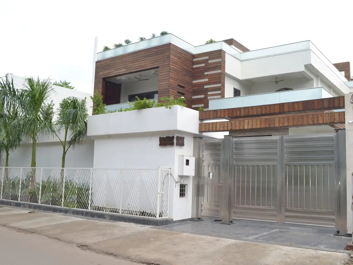Street front with timber-clad upper volumes, a planted terrace, white boundary railing and steel gates