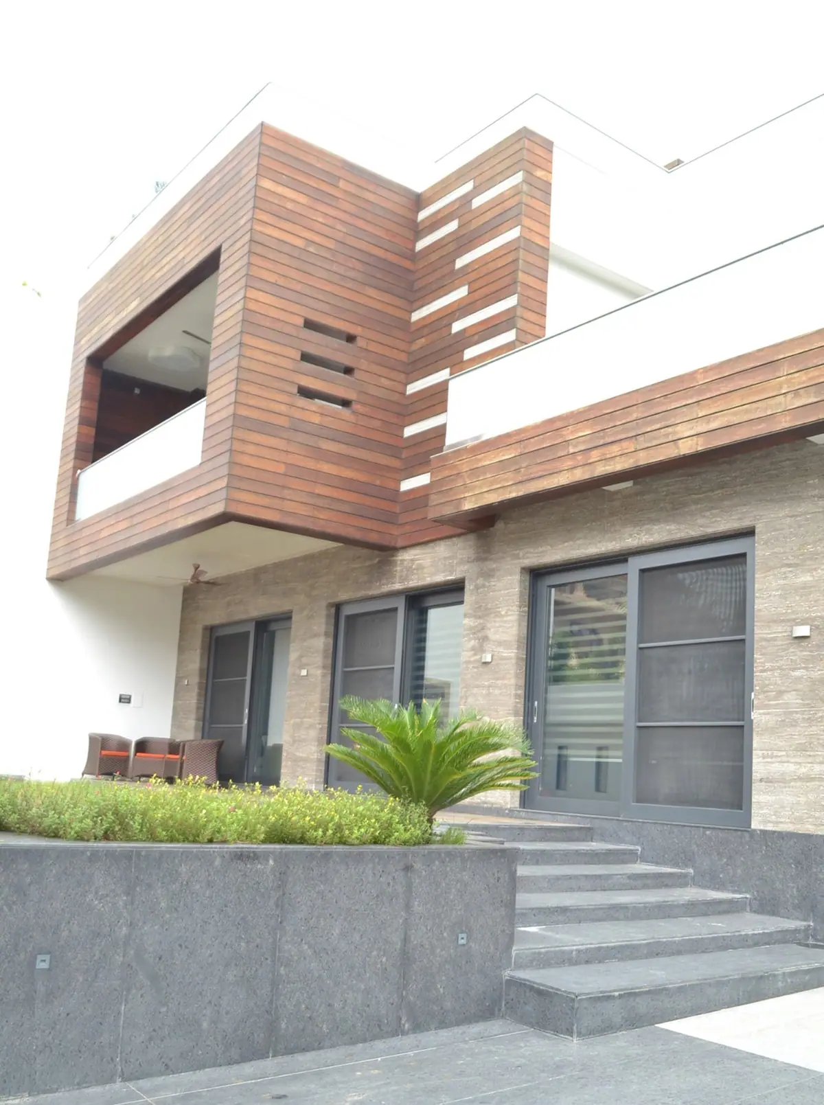 Timber-clad balcony and slotted timber wall rising above the granite planter and steps